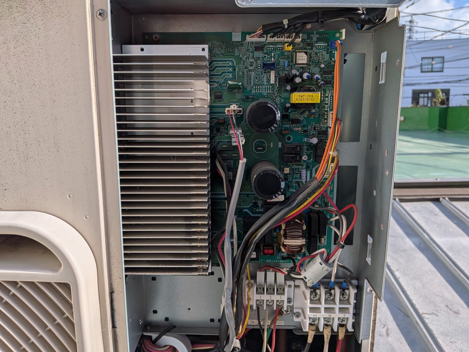 屋根上に設置された東芝室外機の電装ボックスを開けて制御基板を点検する様子（足立区の学習塾）